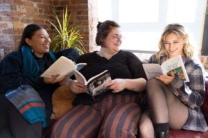 Three people sitting on a couch, each reading a book and smiling.