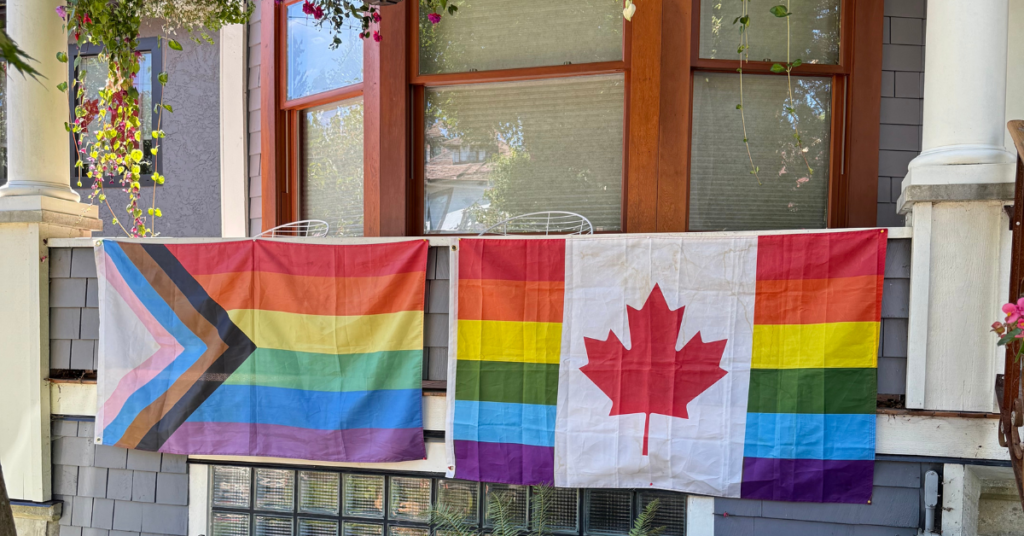 Canadian pride flag with the maple leaf in the middle hanging beside an intersectional Pride flag on a porch in Vancouver, Canada