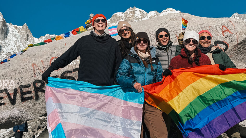 queer travelers hold a Trans and a Pride flag Everest base camp in Nepal after a trek