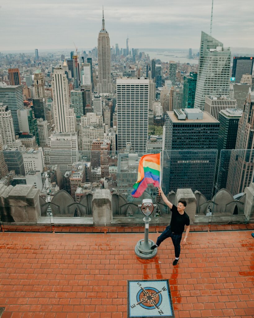 queer woman waving a pride flag in front of the NYC skyline