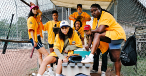 queer people together in a dugout wearing yellow jerseys. they are the characters for the lesbian baseball show, Slo Pitch