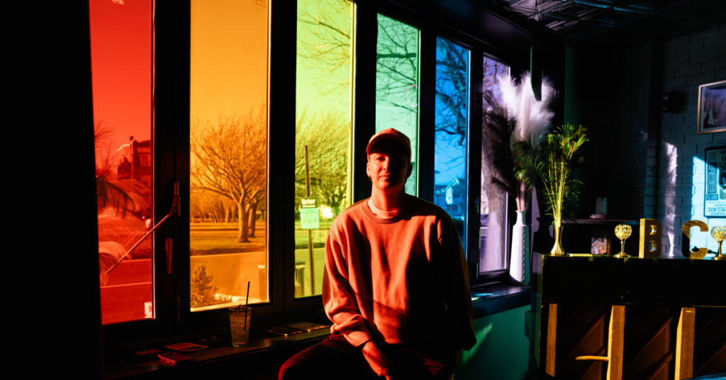gender non conforming traveler sitting in front of a rainbow window