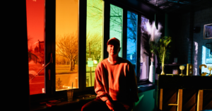 gender non conforming traveler sitting in front of a rainbow window