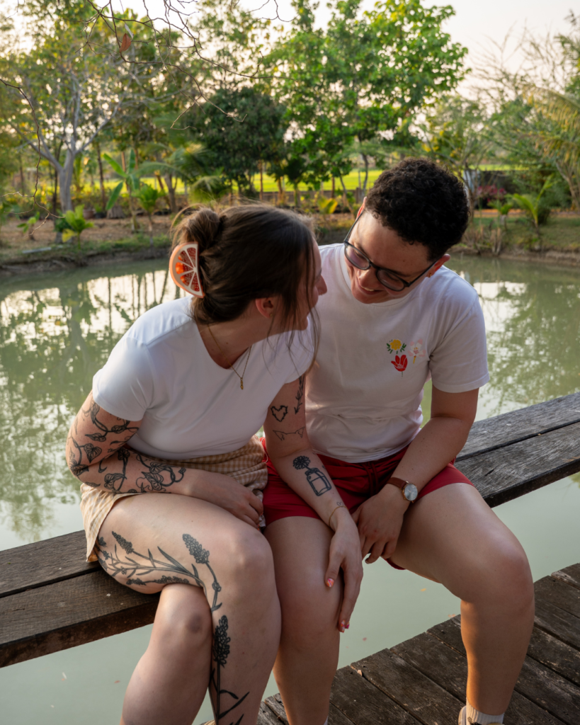 queer couple sitting near a pond laughing together